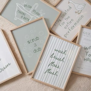 K&ouml;nnte beinhalten: Eine Sammlung gerahmter Badezimmer-Kunstdrucke mit hellen Holzrahmen. Die Drucke zeigen S&auml;tze wie "wash, brush, floss, flush" und "scrub a dub" in handschriftlichem Stil. Die Farbpalette umfasst Gr&uuml;n-, Wei&szlig;- und Graut&ouml;ne.