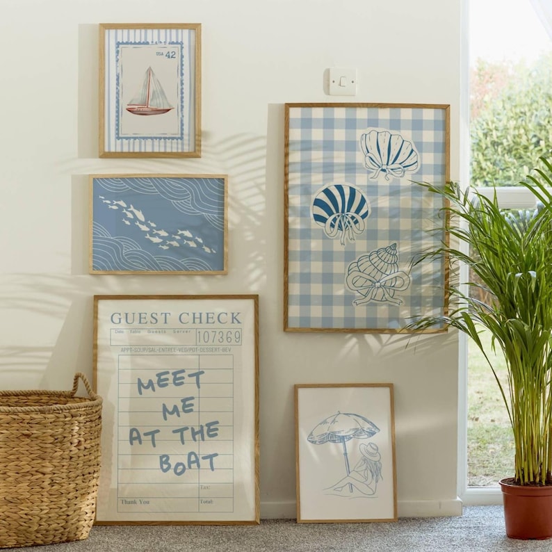 May include: A collection of framed wall art with a nautical theme. The art includes a sailboat, fish, seashells, and a beach scene. One piece has the text "Meet Me At The Boat."