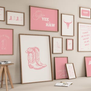 May include: A gallery wall arrangement featuring multiple framed prints with pink and white colour schemes. The artwork includes illustrations of cowboy boots, a cow skull, a surfboard, playing cards, and text such as Yee to the Haw.