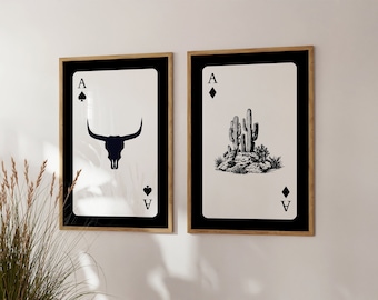 May include: Two framed prints of playing cards with a black and white design. The left print features the Ace of Spades with a bull skull. The right print features the Ace of Diamonds with a cactus.