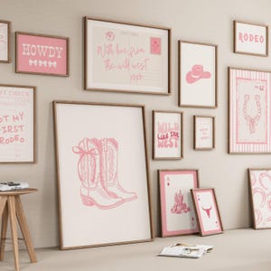 May include: A gallery wall arrangement of multiple framed prints featuring pink and white western-themed illustrations. The collection includes images of cowboy boots, a horseshoe, a cactus, a bull skull, and text such as Howdy and Rodeo.