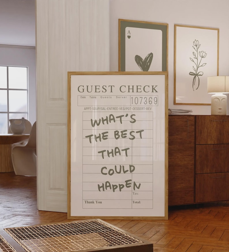 May include: A framed print designed to look like a guest check, featuring the handwritten text "WHAT'S THE BEST THAT COULD HAPPEN". The frame is light brown. Two other framed prints are visible in the background.