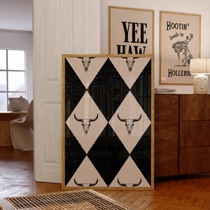 May include: A framed print with a black and white checkered pattern featuring a repeated design of a bull skull. The print is framed in a natural wood frame.