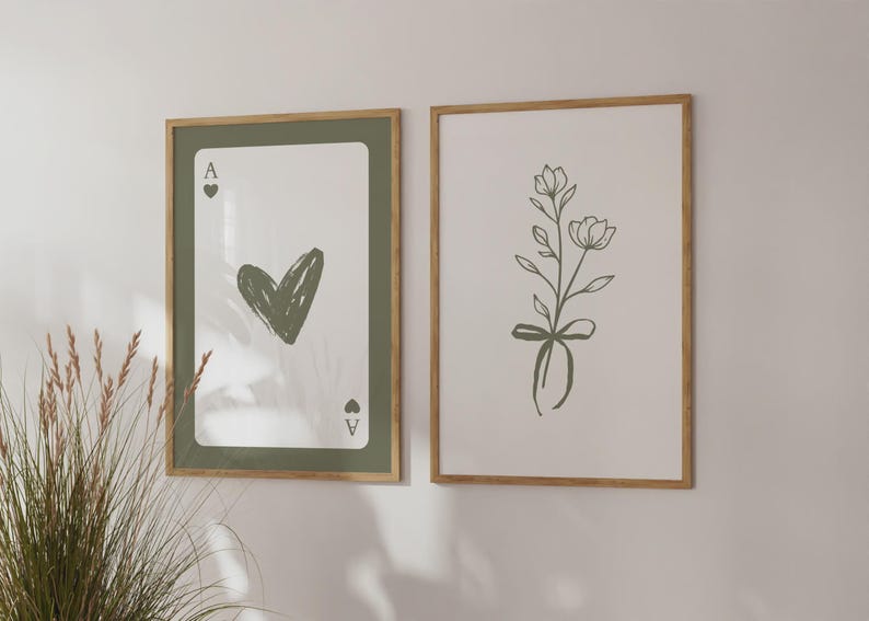 May include: Two framed art prints. One shows an Ace of Hearts playing card design with a green heart. The other print displays a floral illustration with a bow. Both are in wooden frames.