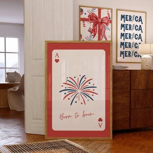 Puede incluir: Una impresi&oacute;n enmarcada de un As de corazones con un borde rojo. La tarjeta presenta un dise&ntilde;o de fuegos artificiales en rojo, blanco y azul, con el texto "Born to boom". Se ven otras impresiones enmarcadas con temas patri&oacute;ticos.