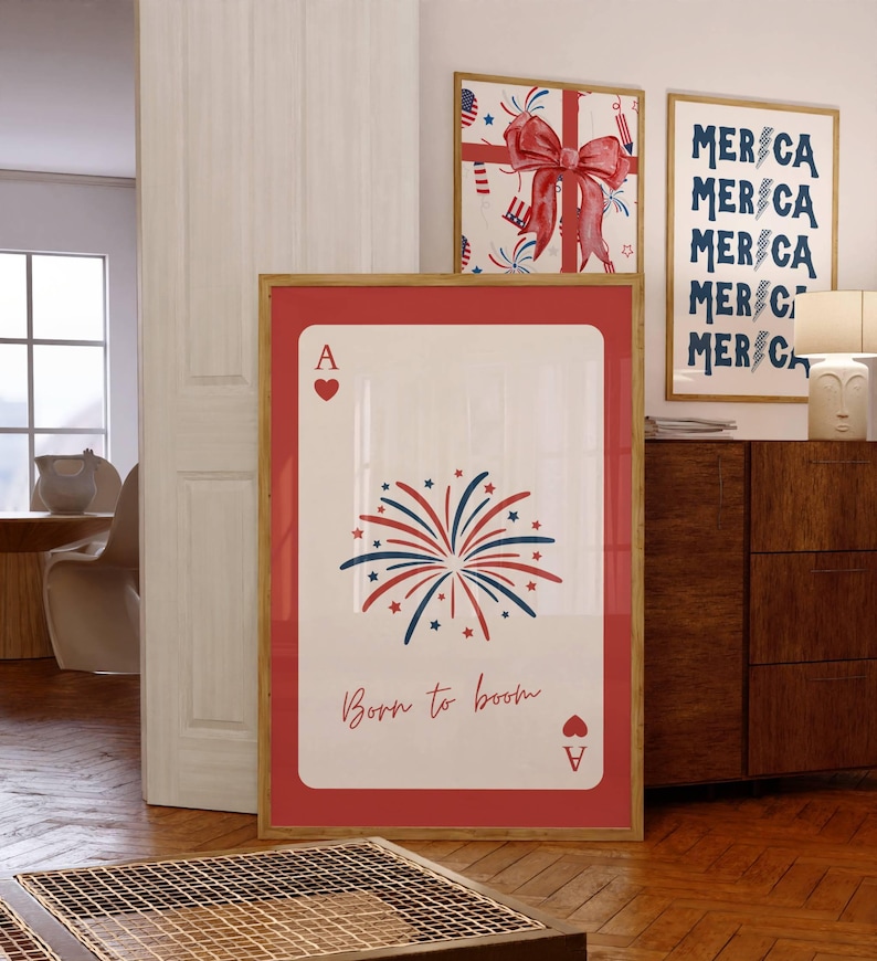 Puede incluir: Una impresi&oacute;n enmarcada de un As de corazones con un borde rojo. La tarjeta presenta un dise&ntilde;o de fuegos artificiales en rojo, blanco y azul, con el texto "Born to boom". Se ven otras impresiones enmarcadas con temas patri&oacute;ticos.