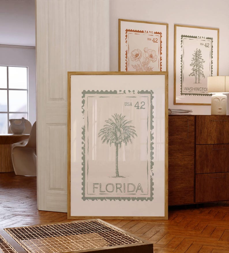 May include: A framed print featuring a palm tree design with the word "FLORIDA" at the bottom. The print is in a light green color and is framed in a light brown wooden frame. Other framed prints with floral and tree designs are visible.