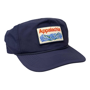 May include: Navy blue cap with a rectangular patch featuring the word "Appalachia" in orange, above a mountain range design in blue and green. The cap has a curved brim and an adjustable rope detail.