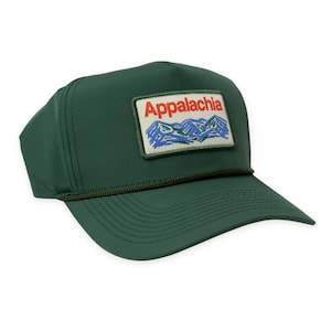 May include: A dark green trucker hat with a rectangular patch featuring the word "Appalachia" in red letters above a mountain range design in blue and white. The hat has a curved brim and a dark green rope detail.