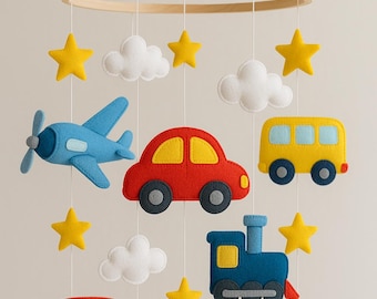 May include: A baby mobile featuring felt cutouts of a blue airplane, red car, yellow bus, red bus, blue truck, and blue train. The mobile also includes yellow stars and white clouds, all suspended from a wooden ring.
