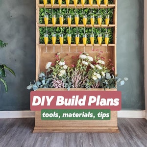 Może przedstawiać: Plany budowy DIY dla drewnianej, ściennej ekspozycji na napoje z zielonym, sztucznym tłem roślinnym i półką wypełnioną przezroczystymi szklankami wypełnionymi pomarańczowym sokiem. Dolna część ekspozycji ma doniczkę wypełnioną białymi i różowymi kwiatami.