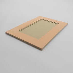 May include: A rectangular, light brown picture frame with a recessed centre. The frame has a simple, clean design with a narrow inner border. The background is a light grey.