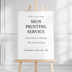 May include: A white rectangular sign displayed on a light-coloured wooden easel. The sign features black text that reads: PRINT YOUR OWN SIGN PRINTING SERVICE, Upload your design, We print & ship, Available in A4 • A3 • A2. The sign is centred.