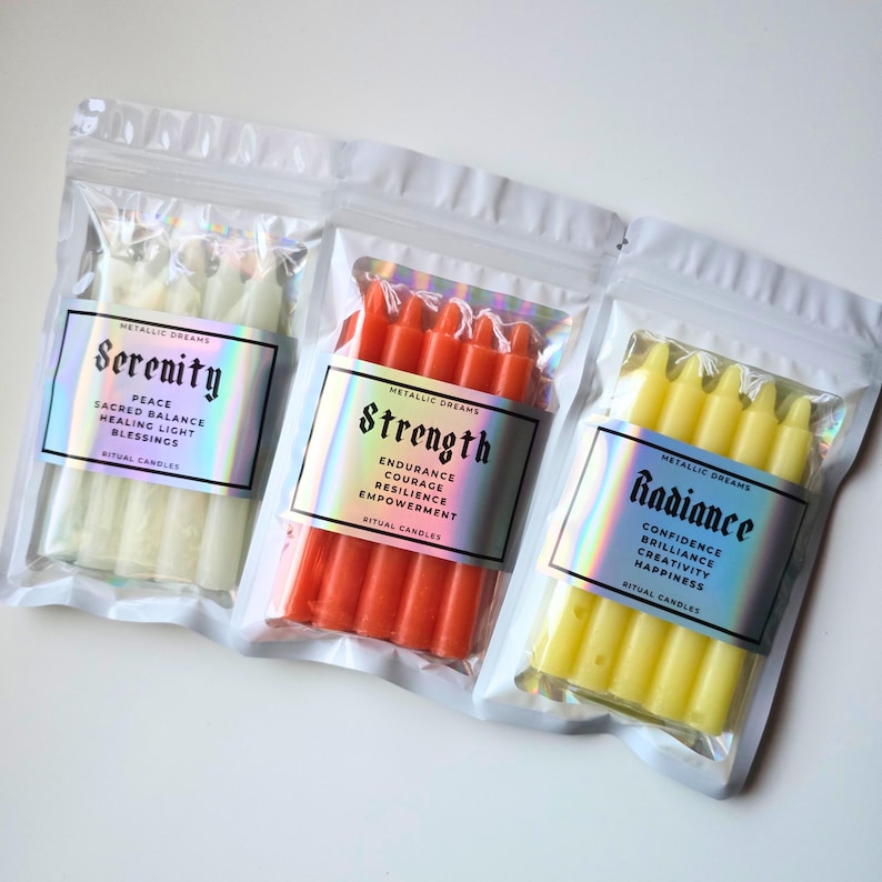 May include: Three clear resealable pouches containing ritual candles. The left pouch holds white candles labeled Serenity, the center holds orange candles labeled Strength, and the right holds yellow candles labeled Radiance. Each label features holographic text.