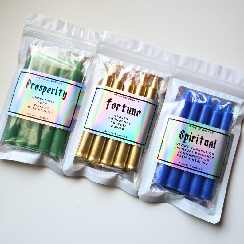 May include: Three sealed plastic bags containing ritual candles. One bag holds green candles labeled "Prosperity", another holds gold candles labeled "Fortune", and the third contains blue candles labeled "Spiritual". Each bag has a holographic label.