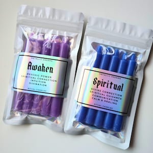 May include: Two packages of ritual candles. One contains purple candles labeled "Awaken" with text about psychic power and intuition. The other has blue candles labeled "Spiritual" with text about divine connection and healing.