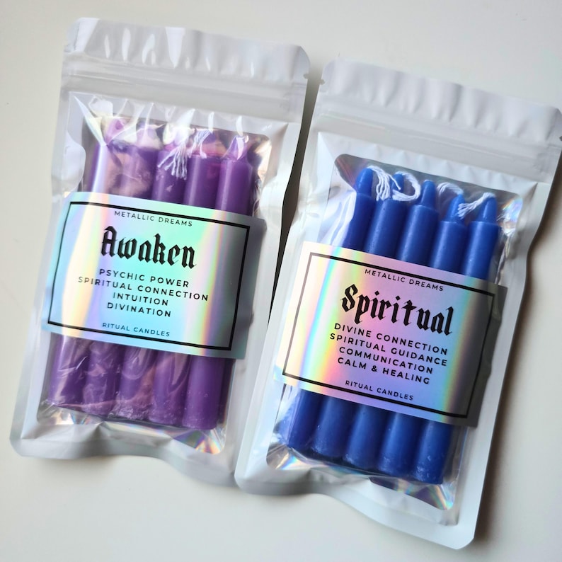 May include: Two packages of ritual candles. One contains purple candles labeled "Awaken" with text about psychic power and intuition. The other has blue candles labeled "Spiritual" with text about divine connection and healing.