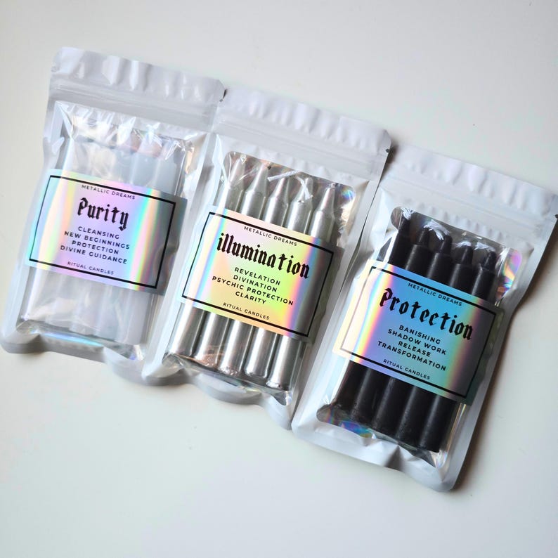 May include: Three sealed bags of ritual candles. The bags have iridescent labels with the words "Purity", "Illumination", and "Protection". Each label lists associated intentions. The "Purity" candles are white, "Illumination" are silver, and "Protection" are black.