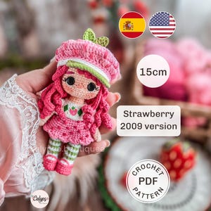 Puede incluir: Una muñeca de ganchillo de 15cm de altura, con pelo rosa, un gorro rosa con hojas verdes y un vestido blanco con estampado de fresas. La muñeca tiene grandes ojos negros, mallas a rayas verdes y blancas y zapatos rosas. Texto: Strawberry 2009 version y CROCHET PDF PATTERN.