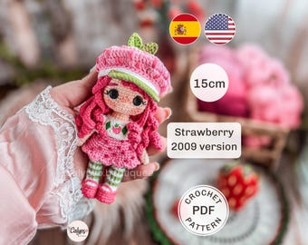 May include: A crochet doll measuring 15cm in height, featuring pink hair, a pink hat with green leaves, and a white dress with a strawberry print. The doll has large black eyes and wears green and white striped leggings with pink shoes. Text reads Strawberry 2009 version and CROCHET PDF PATTERN.