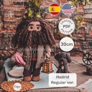 Puede incluir: Una muñeca de ganchillo con pelo largo castaño y barba, vistiendo una chaqueta marrón y pantalones oscuros. La muñeca sostiene un paraguas rosa y un farol marrón. Junto a ella hay un pequeño perro de ganchillo marrón. El texto indica 30cm.