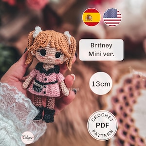 May include: A crochet doll with light brown hair in pigtails, wearing a pink dress with a black collar and black boots. The doll features large dark eyes and white hair accessories. Text on the image reads Britney Mini ver. 13cm CROCHET PDF PATTERN.