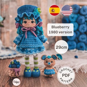 Peut inclure: Une poupée crochetée à la main avec des cheveux bleus, une robe bleue, un chapeau assorti avec des baies, et des leggings rayés vert et blanc. La poupée mesure 29cm de haut, accompagnée d'un petit panier de myrtilles et d'une souris en crochet.