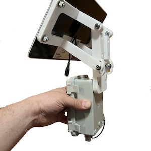 May include: A white solar panel mounted on a white adjustable bracket. The panel is connected to a gray box with a black cable. The box has a black cable coming out of the bottom.
