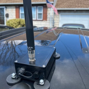 May include: A black Alfa 915 antenna mounted on a black car roof with a magnetic base. The antenna is connected to a black box with a cable and two connectors.