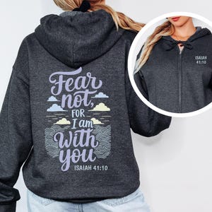 Puede incluir: Sudadera con capucha gris oscuro con cremallera y el texto "Fear not, for I am with you" y "Isaías 41:10" impreso en la espalda. La sudadera también tiene el texto "Isaías 41:10" impreso en la parte delantera. El diseño incluye nubes y patrones de olas.