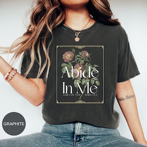 May include: A dark gray t-shirt with a floral design and the text "Abide In Me and I in You John 15:4".