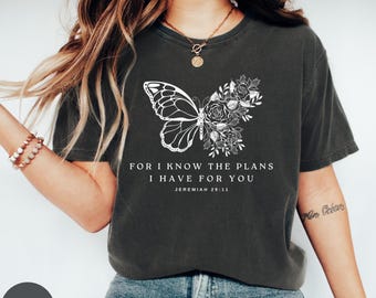 May include: A charcoal grey t-shirt featuring a white butterfly and floral design. The shirt has the text "For I know the plans I have for you Jeremiah 29:11" printed on it.