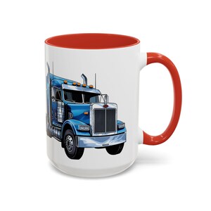 Puede incluir: Una taza de café de cerámica blanca con interior y asa rojos. La taza presenta una ilustración de dibujos animados de un camión semirremolque azul.