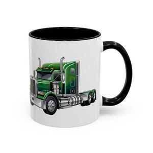 Op de afbeelding: Een witte keramische koffiemok met een zwarte rand en handvat. De mok heeft een cartoonillustratie van een groene vrachtwagen.