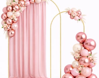 May include: A gold metal arch backdrop stand draped with a light pink fabric curtain, decorated with a cluster of metallic rose gold, matte pink, and cream balloons, along with small white floral accents arranged on the frame.