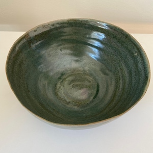 May include: A large, green ceramic bowl with a swirling glaze pattern. The bowl is handmade and has a rustic, organic feel.