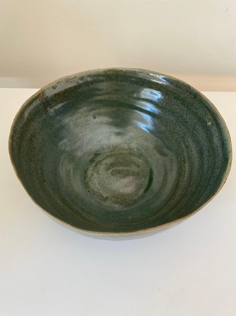 May include: A large, green ceramic bowl with a swirling glaze pattern. The bowl is handmade and has a rustic, organic feel.