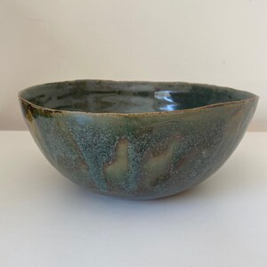 May include: A large, green ceramic bowl with a speckled glaze. The bowl has a wide, rounded shape and a slightly uneven rim.
