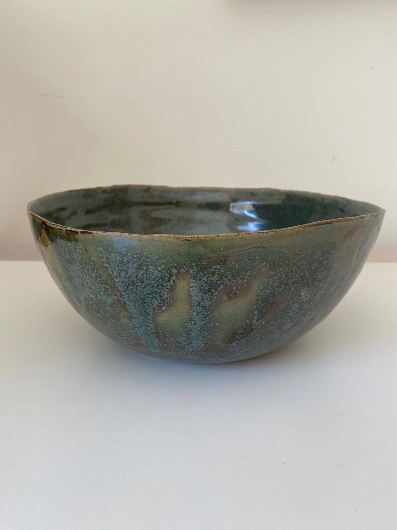 May include: A large, green ceramic bowl with a speckled glaze. The bowl has a wide, rounded shape and a slightly uneven rim.