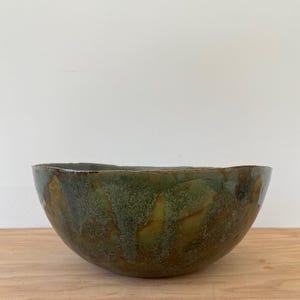 May include: A large, green and brown ceramic bowl with a speckled glaze. The bowl has an uneven, organic shape.