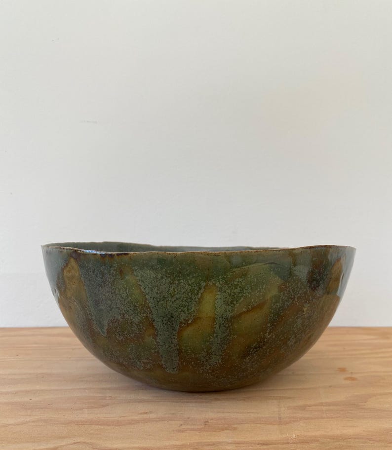 May include: A large, green and brown ceramic bowl with a speckled glaze. The bowl has an uneven, organic shape.