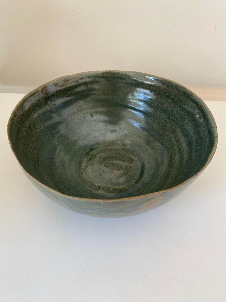 May include: A large, green ceramic bowl with a swirling pattern. The bowl has a wide rim and a deep, rounded interior.