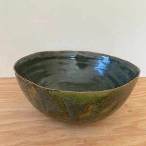 May include: A green ceramic bowl with a speckled glaze. The bowl has a rounded shape and a wide rim.