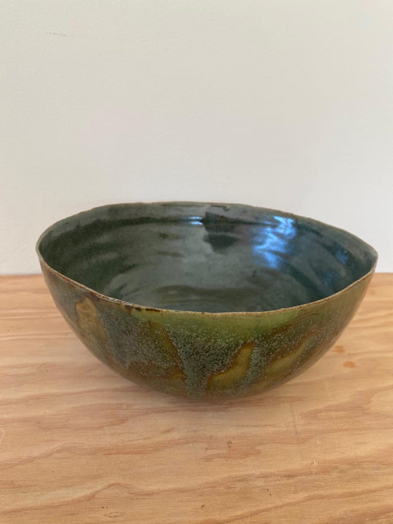 May include: A green ceramic bowl with a speckled glaze. The bowl has a rounded shape and a wide rim.