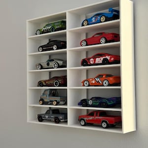 May include: White wall-mounted shelf unit with 10 slots for displaying toy cars. The shelves are filled with a variety of toy cars in different colours, including red, blue, green, and black.