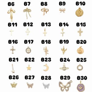 May include: A selection of small, decorative charms in various shapes, including bows, crosses, stars, moons, butterflies, and a planet. The charms are gold-toned and some are embellished with crystals or coloured enamel.