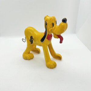 Könnte beinhalten: Eine gelbe Vintage-Pluto-Figur mit schwarzer Nase, Ohren und rotem Halsband. Die Hundefigur hat eine rote Zunge, die herausragt, und steht auf allen Vieren. Ein klassisches Disney-Sammlerstück.