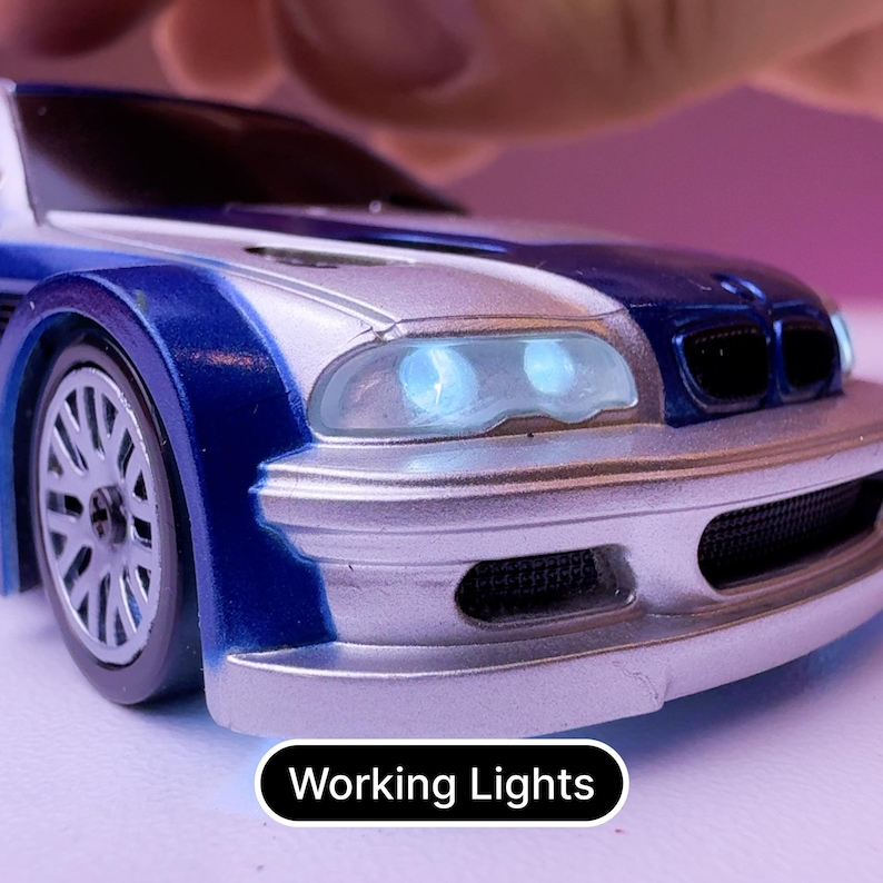 May include: A silver and blue toy car with working headlights. The car has a black grill and a blue stripe down the side.