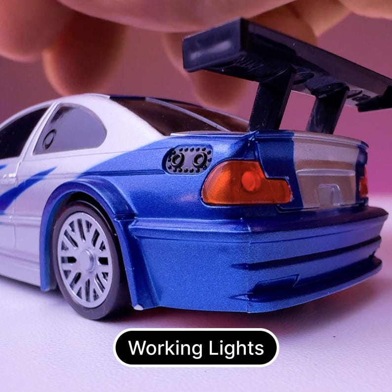 May include: A blue and white toy car with a black spoiler and working lights. The car has a silver trim and a black rear bumper.