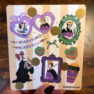 K&ouml;nnte beinhalten: Ein Stickerbogen mit cremefarbenem und goldfarbenem gestreiftem Hintergrund mit Illustrationen von Schneewittchen, der b&ouml;sen K&ouml;nigin und anderen Elementen aus dem Disney-Film. Der Text "MIRROROOO" ist ebenfalls vorhanden. Der Stickerbogen wird von einer Person gehalten.